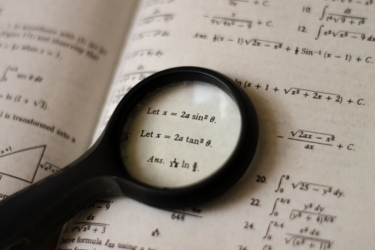 services-01 A magnifying glass focusing on mathematical equations in a textbook, symbolizing detailed study.