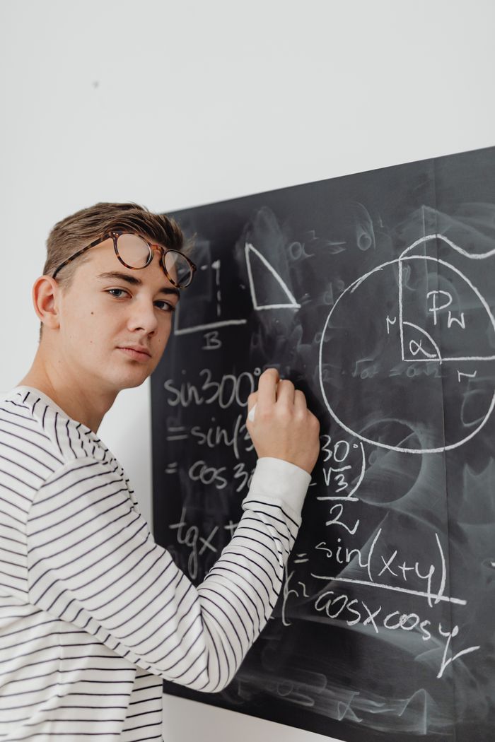 services-02 Teenager writing mathematical equations on blackboard, focused learning.