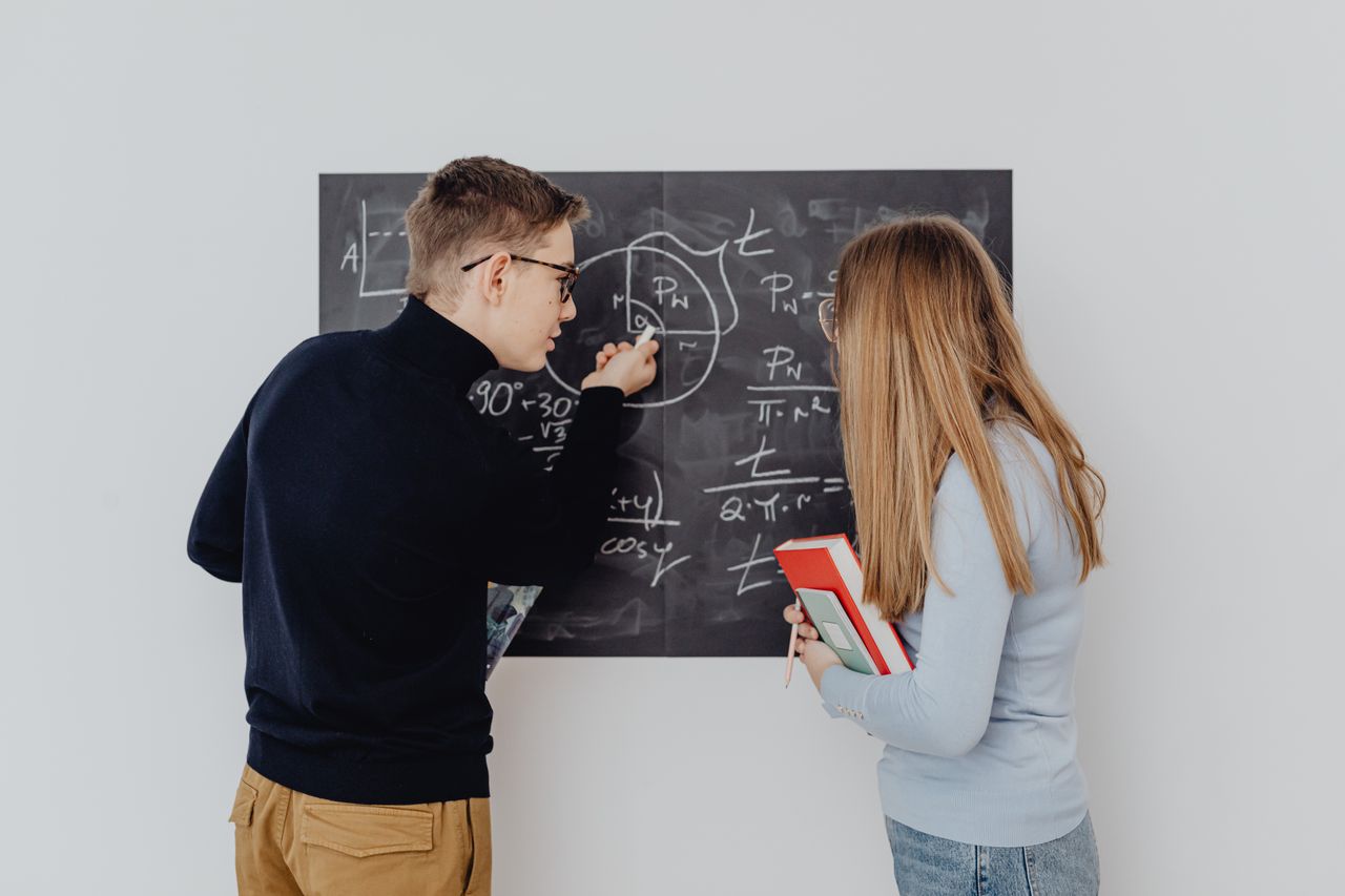 Two students working together on trigonometric equations on a blackboard, enhancing learning.