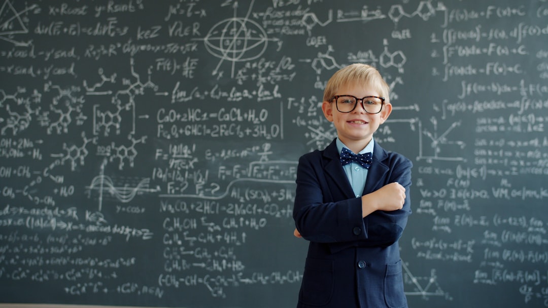 team-01 Happy kid in suit and glasses is standing in class with chalkboard in background with scientific formulas written on it. People, childhood and education concept.