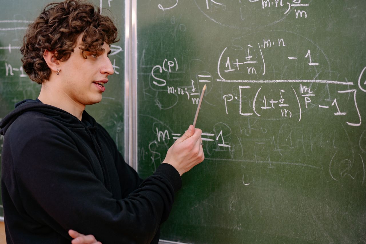 team-02 A young male educator explaining complex math equations at a university classroom blackboard.